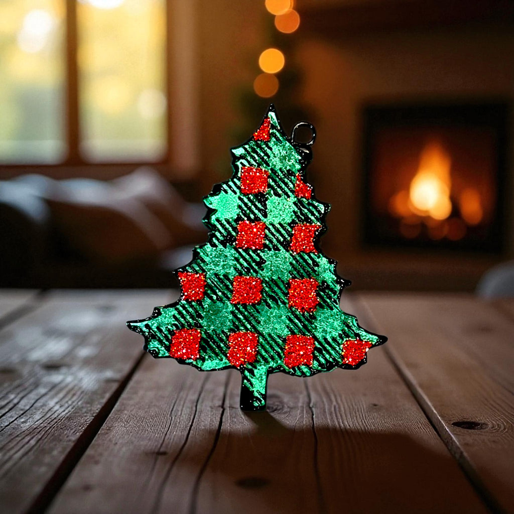 Decorative Christmas tree car freshie in green with red glitter on a wooden surface with a fireplace in the background