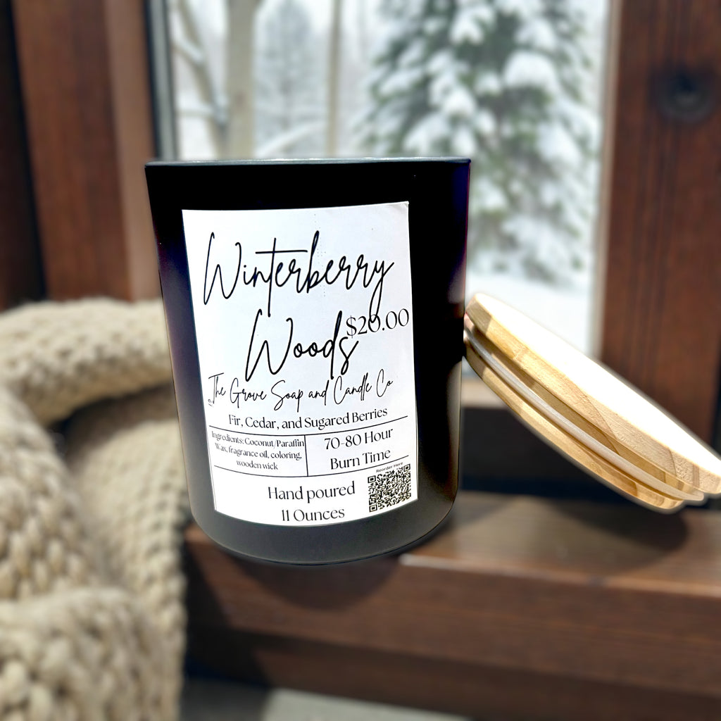 Candle labeled 'Winterberry Woods' so that you can see the scent of fir, cedar wood, and frosted berries on a surface with a blurred background