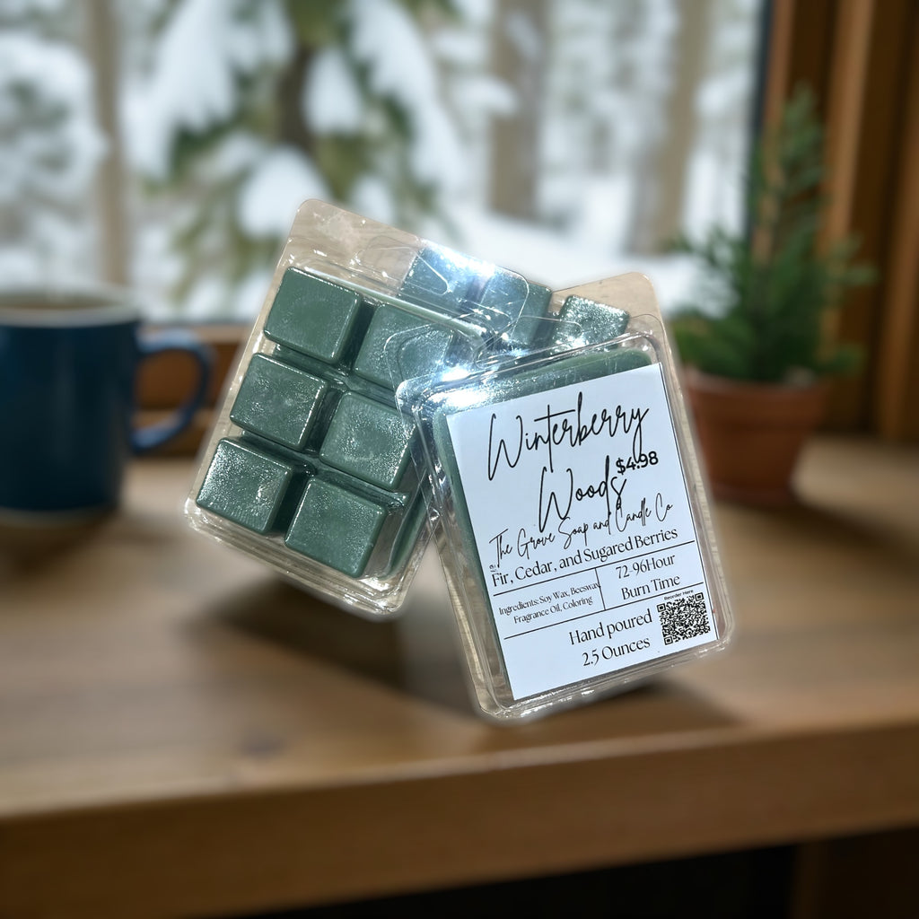Packaged clamshell wax melts with a label showing company name of The Grove Soap and Candle Co and the scent profile of Winterberry Woods on a wooden surface, blurred background