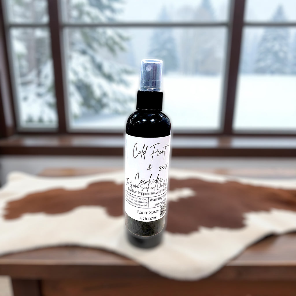 Bottle of room spray with the label Cold Front & Cowhides on a wooden surface with a snowy window background