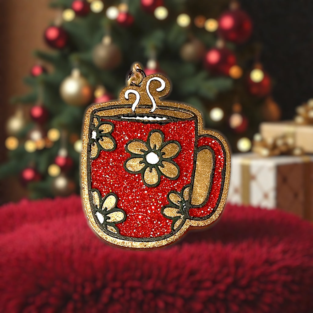 Decorative red glitter mug car freshie with gold accents on a red surface with a Christmas tree in the background.