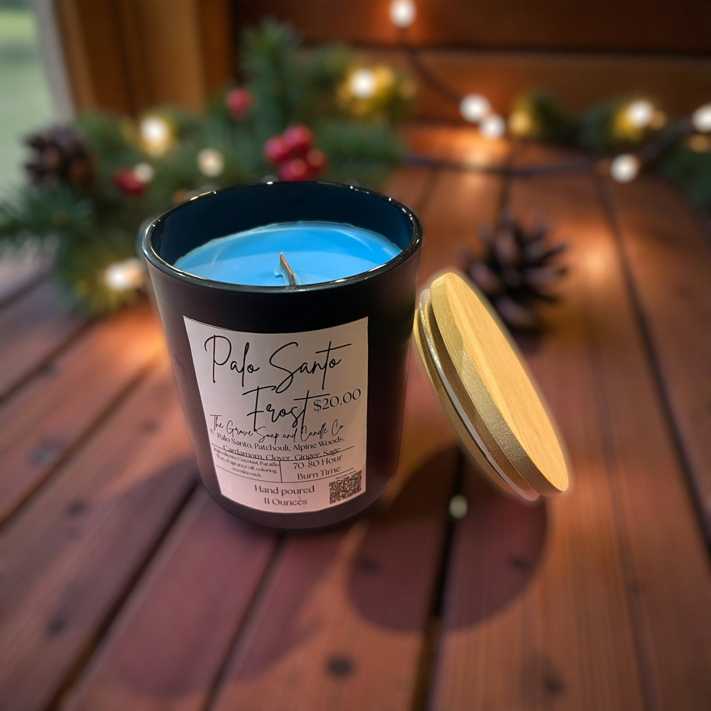 Blue candle Palo Santo Frost in a black container with a label on a wooden surface, surrounded by festive decorations.