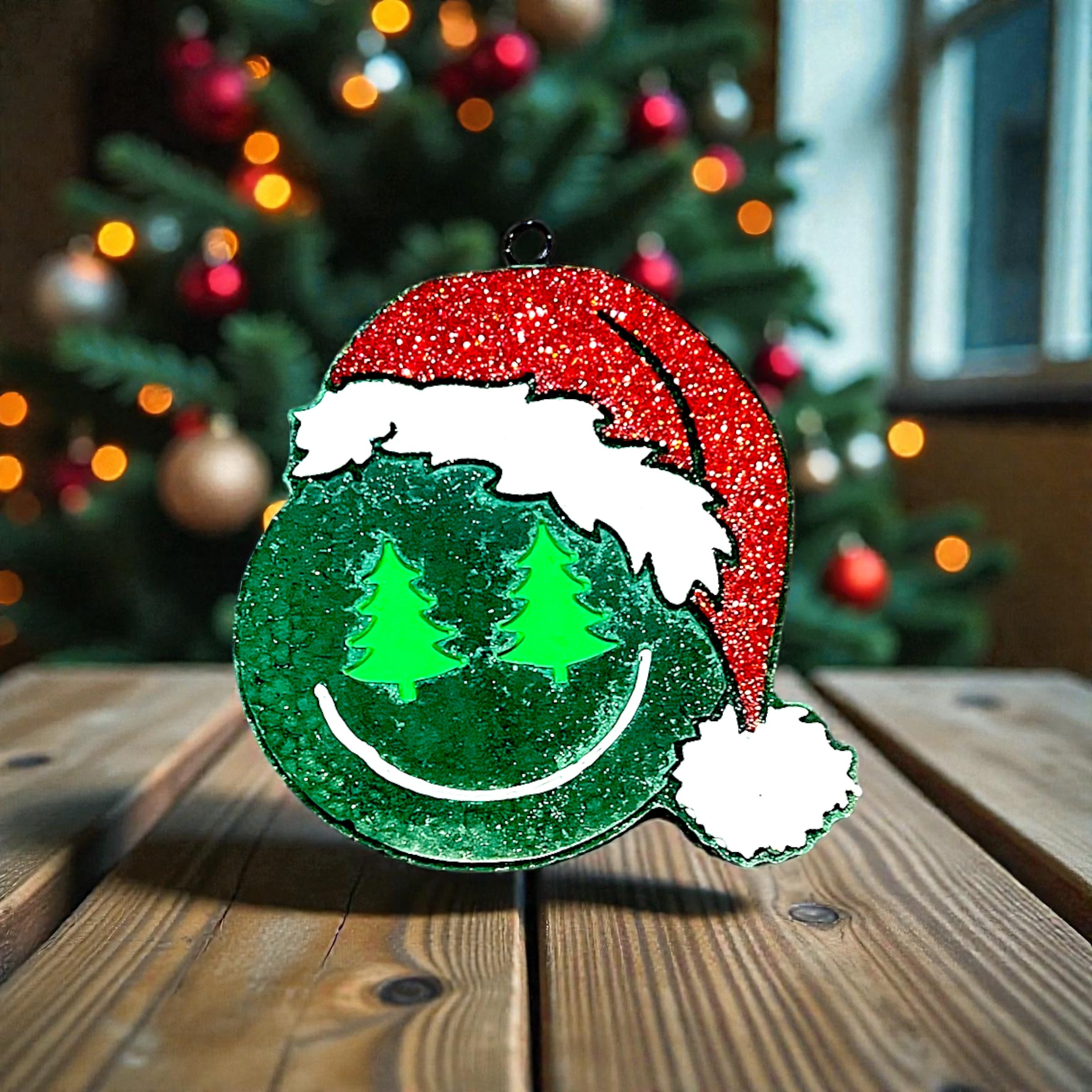 Decorative Christmas car freshie with a smiley face and Santa hat on a wooden surface with a blurred Christmas tree in the background.