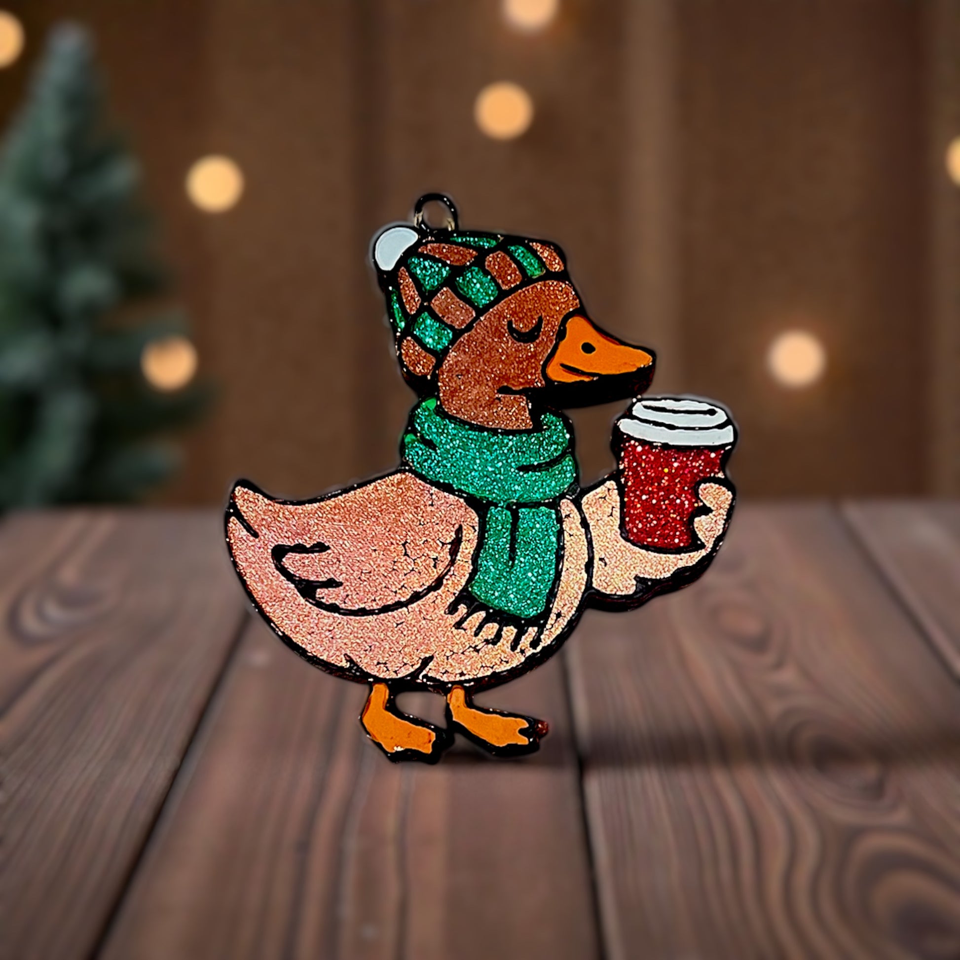 Decorative duck car freshie with a hat and scarf, holding a mug, on a wooden surface.