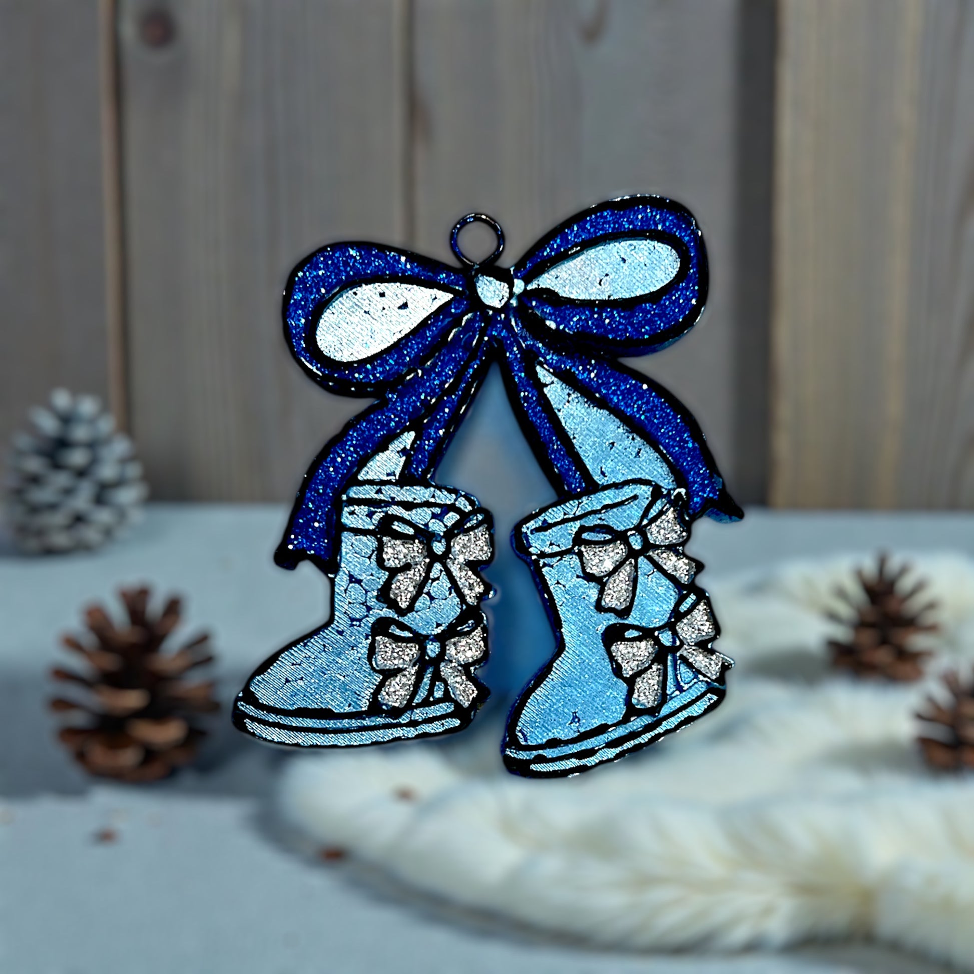 Decorative winter boot car freshie with a glitter blue bow on top and glitter silver bows accenting the back of the boot on a wooden surface.